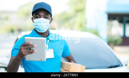 Delivery african postman in blue uniform holding package with wearing facemask Stock Photo