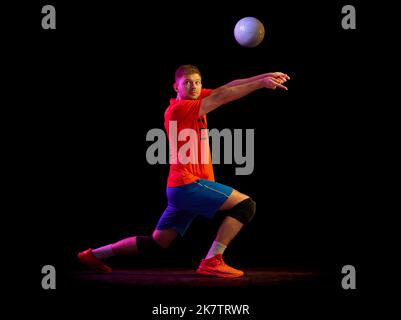 Dynamic portrait of male volleyball player training with ball isolated on dark background in neon light. Sport, gym, team sport, challenges Stock Photo