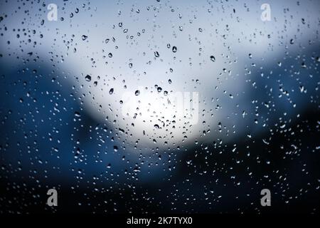 Raindrops on window glass on blue background. Selective focus. Rainy city background Stock Photo