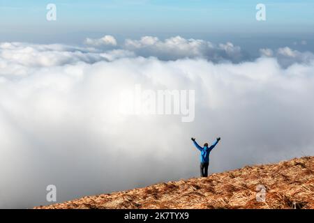 Alone tourist on the edge of the cliff against the backdrop of an incredible foggy sea. Ocean of fog in sunrise mountains landscape. Travel concept Stock Photo