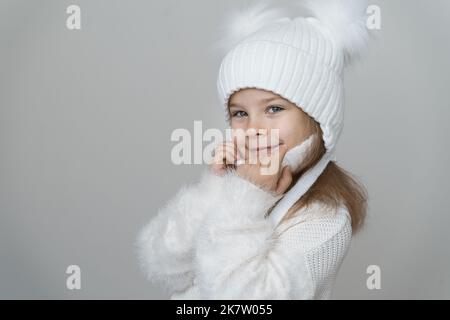 trendy warm winter - beautiful kid girl in white wool winter hat and knitted sweater. Portrait of beauty winter girl in woolen clothing. Stock Photo