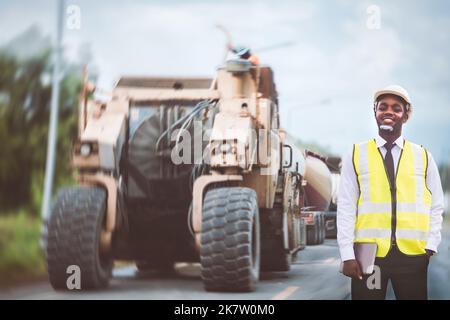 African engineer man or architect checking construction with white safety helmet in construction site. Standing at highway concrete road site Stock Photo