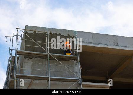 Worker plastering the outside of a building with cement on the scaffolding. Work Safety concept photo. Stock Photo