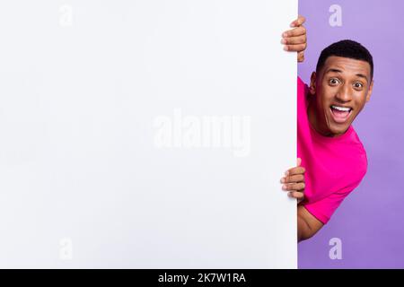 Photo of cheerful nice man wear stylish pink clothes hand hold empty space head behind big board isolated on purple color background Stock Photo