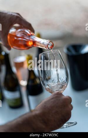 Close up of a man pouring a bottle of rose wine into a wine glass Stock Photo