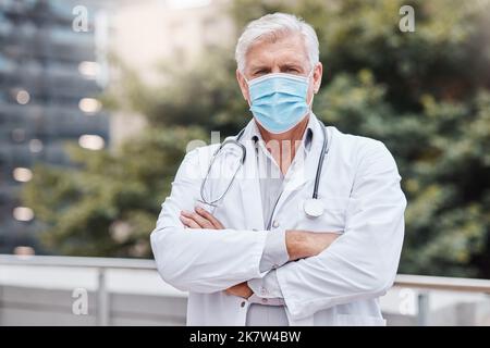 Get serious about wearing your mask. a mature male doctor standing with his arms crossed in the city. Stock Photo