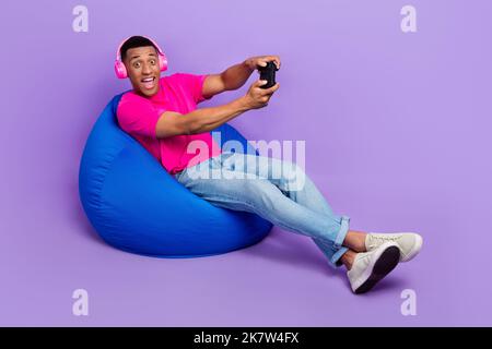 Photo of positive astonished man stylish outfit sit comfort chair have fun enjoy free time empty space isolated on purple color background Stock Photo