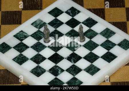 King and Queen chess pieces on a black and white marble chess board looking at each other. A Symbolic Couple. metal chess pieces. Stock Photo