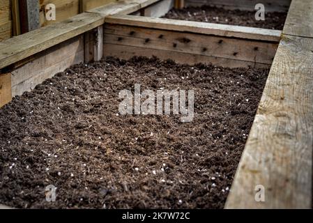 Closeup of big wooden planter vegetable box container in garden filled with soil ready for planting seeds and plants. Stock Photo