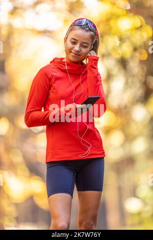 Young female athlete in sportswear listens to music on smartphone and puts headphones before running. Stock Photo