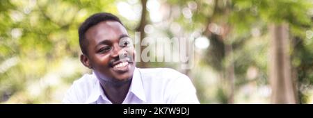 African man in a white shirt sits and laughs happily in the park. Concept of positive thinking and happy living Stock Photo