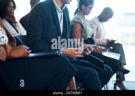 We get bored without instant gratification. a group of young businesspeople using cellphones during a a meeting in a modern office. Stock Photo