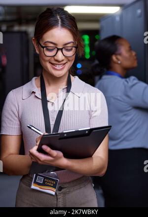 Server maintenance in progress. an attractive young female programmer working in a server room with her colleague in the background. Stock Photo