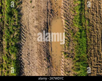 Aerial view of a dirty dirt road with mud, grass and tracks between fields and fields in autumn Stock Photo