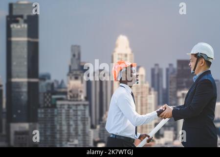 Smiling african engineer and asian construction managers shaking hands at construction site with the tower in background. Concept of  team workers con Stock Photo