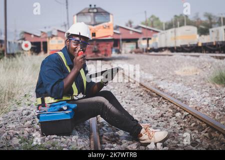 African man  technician engineer check and repair the train on railway with holding tablet and talking by radio communication or walkie talkie Stock Photo