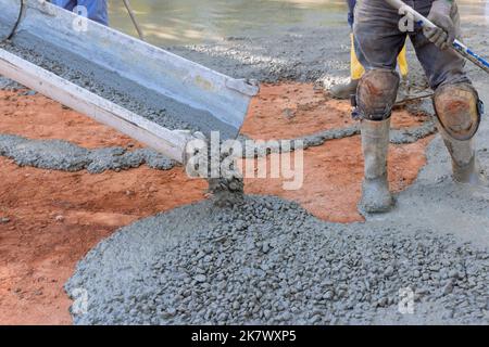 Concrete contractor pours wet concrete during the paving driveway while he is working on it Stock Photo