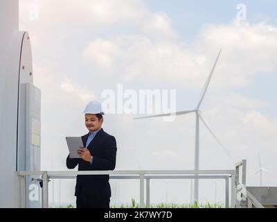 Asian engineer in a suit is using a tablet to control and monitor the operation of a wind turbine in the electrical control room.Concept of sustainabi Stock Photo