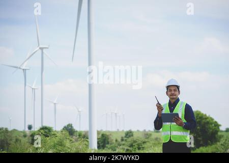Engineer man stand holding tablet front the wind turbines generating electricity power station. Concept of sustainability development by alternative e Stock Photo