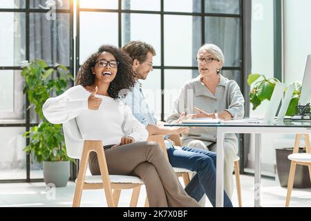 woman giving a thumbs up while sitting near an office desk. Stock Photo