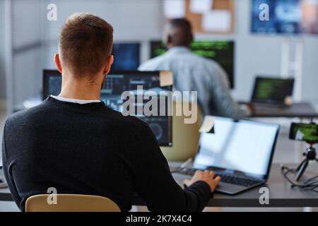 Back view of male programmer or data specialist using computer in office with charts on screen, copy space Stock Photo
