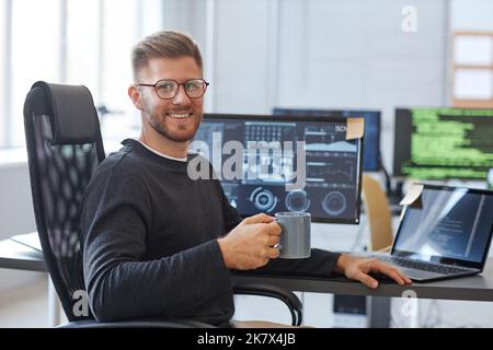 Portrait of software programmer smiling at camera while posing at workplace in office with coffee cup, copy space Stock Photo