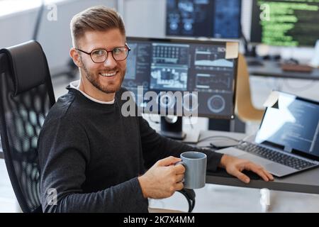 Portrait of young software engineer smiling at camera while posing at workplace in office with coffee cup, copy space Stock Photo
