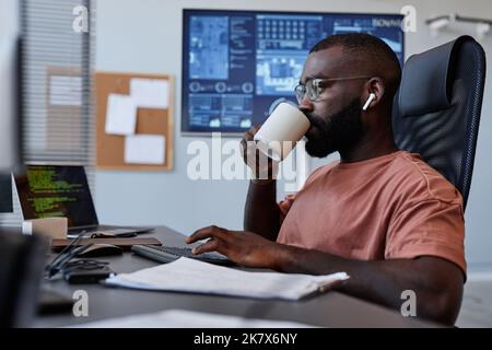 Side view portrait of black man drinking coffee at workplace while working in IT software development Stock Photo