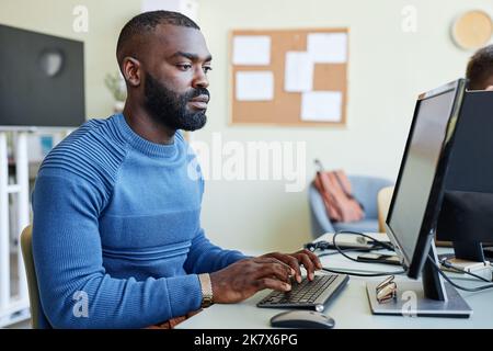 Side view portrait of bearded black man using laptop in office while programming software Stock Photo
