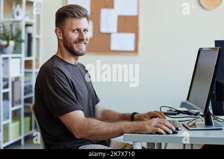Portrait of young computer programmer looking at camera and smiling while writing code at home office workplace Stock Photo