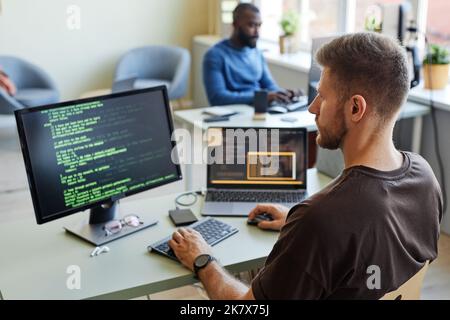 Portrait of software engineer writing code at workplace in office with multiple devices Stock Photo