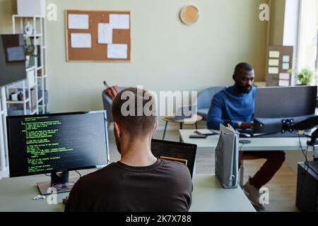 Background image of IT company office with man writing code in green lines, copy space Stock Photo