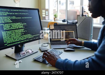 Close up of black software developer writing code at workplace in office with multiple devices Stock Photo
