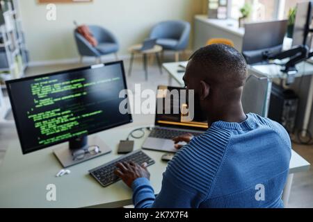 Back view of African American software developer writing code at workplace in office with multiple devices Stock Photo