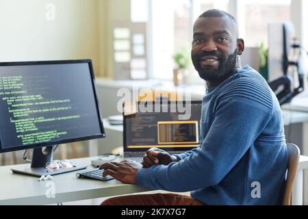 Portrait of black man as computer programmer looking at camera while writing code at office workplace Stock Photo
