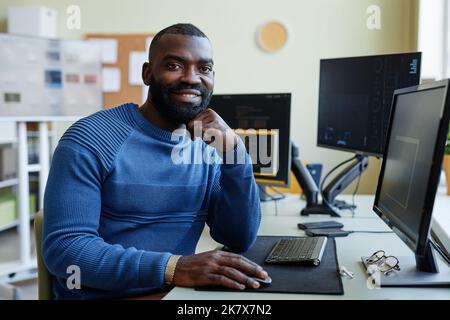 Portrait of African American man as computer programmer smiling at camera while writing code at office workplace Stock Photo