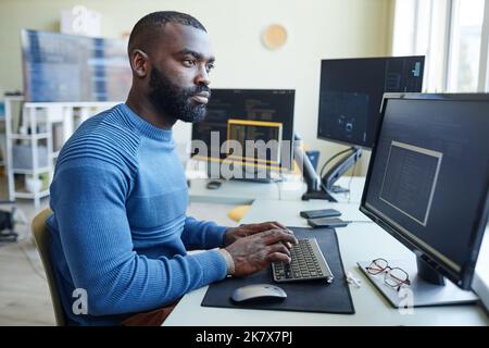 Side view portrait of African American man as computer programmer writing code at office workplace Stock Photo