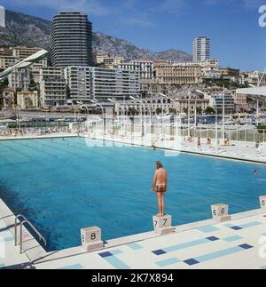 1964, historical, a view of the State Nautique Rainier III, a swimming pool in the middle of Port Hercules in Monaco, with a main diving platform (not in picture) and smaller, stone platforms pool side, one of which a male swimmer is standing on. The open-air Olympic sized seawater pool was officially opened August 1961. Stock Photo