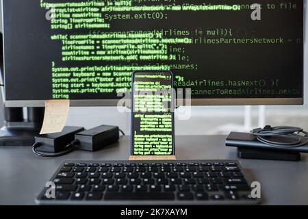 Background image of computer screen with green code lines, focus on smartphone in foreground, copy space Stock Photo