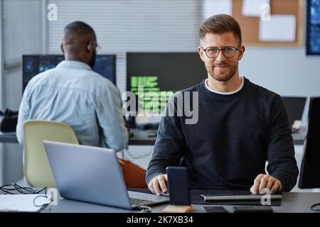 Portrait of male software developer smiling at camera while sitting at workplace in office, copy space Stock Photo