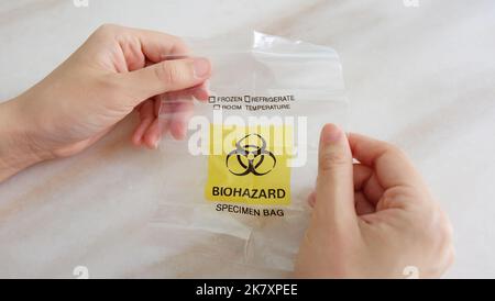 Hands holding a new and empty medical specimen waste bag with the yellow biohazard symbol printed in front. Stock Photo