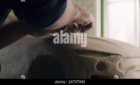 Closeup hands of a car designer works on the design details of an unfinished sculpture of the prototype eco-friendly electric car model. Hand made car sculpture on a wooden table. Stock Photo
