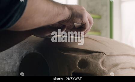 Closeup hands of a car designer works on the design details of an unfinished sculpture of the prototype eco-friendly electric car model. Hand made car sculpture on a wooden table. Stock Photo
