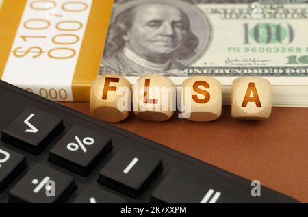 Business concept. On a brown surface are dollars, a calculator and wooden cubes with the inscription - FLSA Stock Photo