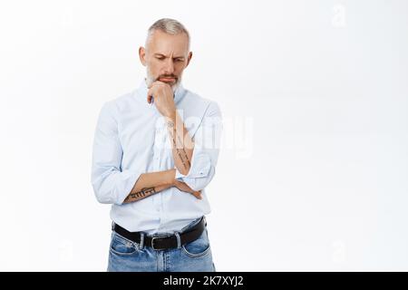 Thoughtful businessman looking down and thinking, pondering with serious face expression, making decision, standing over white background Stock Photo