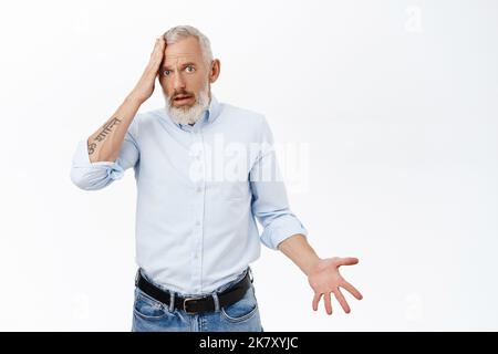 Shocked senior businessman holding hand on forehead and staring puzzled, confused and stunned, standing against white background Stock Photo