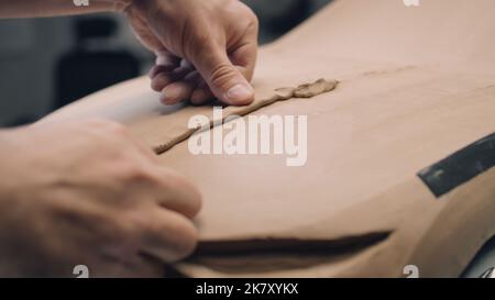 Close-up shot of male automotive designer working on futuristic car model from plasticine clay. Future design of new generation electric car. Work in modern car design studio. Stock Photo