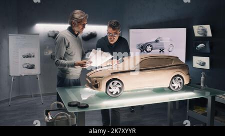 Two male automotive designers working on eco friendly model of electric car in modern car design studio. One sculpting with plasticine clay, other working in 3D modeling computer software. Stock Photo