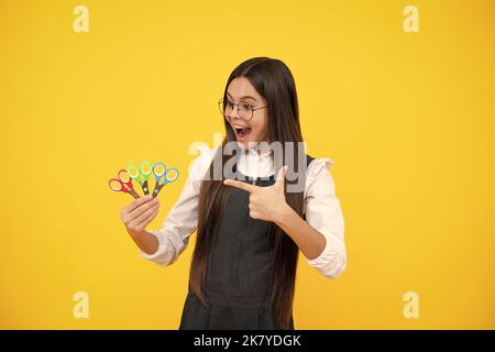 Childrens creativity, arts and crafts. Teenage girl with scissors, isolated on yellow background. Stock Photo