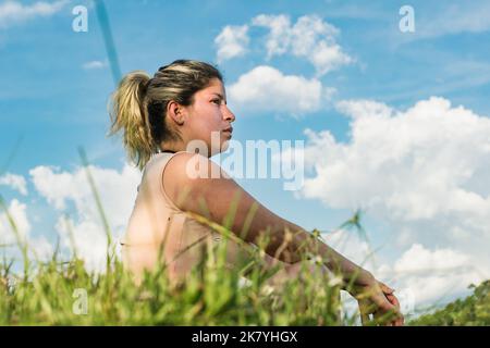 beautiful caucasian latina girl, sitting on top of a mountain looking at the natural beauty of colombia. blue sky background with white summer clouds. Stock Photo